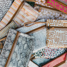Load image into Gallery viewer, Thandana's Sticky Fingers Clear Pouch in Dazzling Blue features a range of laminated fabric patterns, including stripes, polka dots, abstract shapes, and textured prints. Overlapping designs come in earthy tones to vibrant pinks and yellows.