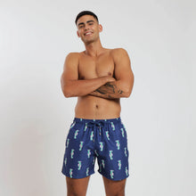 Load image into Gallery viewer, Breazies men swim shorts with green and pink sea horses on a navy background - shown on model crossing his arms smiling