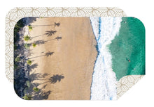 Load image into Gallery viewer, The Bobums Beach Towel - Beach View features an aerial beach scene with turquoise waves, sandy shore, palm tree shadows, and four swimmers. This rectangular microfibre towel has rounded corners, a patterned border, and dries quickly.