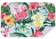 Load image into Gallery viewer, The Bobums Beach Towel - Spring Flamingo features a vibrant tropical design with pink flamingos, yellow and pink hibiscus flowers, blue and white orchids, and lush green palm leaves on a light blue background. Crafted from 100% recycled materials, the beach towel's bottom right corner is turned up like a page curl.