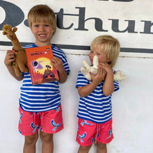 Load image into Gallery viewer, Two young children in matching Breazies Kids Swim Shorts - Lilac Breasted Roller | Coral and pink tops smile. One holds a WALL-E book and a knitted llama, while the other hugs a knitted rabbit, posing against a wall with partial text, ready for aquatic adventures.