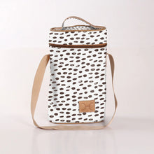 Load image into Gallery viewer, The "Beachy Seeds" lunch bag by Thandana is a white insulated tote with a brown spot pattern and crafted from water-resistant fabric. It features a tan top handle, matching shoulder strap, and a small brown square patch on the bottom front. The background is solid white.