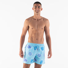 Load image into Gallery viewer, A smiling man stands shirtless against a white background, wearing Breazies Adult Swim Shorts - Turtles in baby blue, made from recycled polyester. He faces forward with his arms relaxed at his sides.