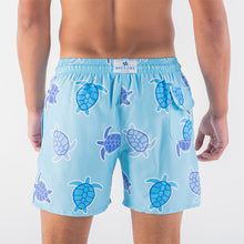 Load image into Gallery viewer, A person is seen from behind wearing Breazies Adult Swim Shorts - Turtles in baby blue, featuring a blue and purple sea turtle pattern against a plain white background.