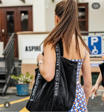 Load image into Gallery viewer, A woman in a colorful, patterned sleeveless dress with long hair carries a black Koko Active bag over her shoulder. She walks through the parking area, exuding style and ease akin to ethically designed Shorty Shorts - The Court by Koko Active.
