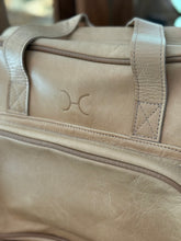 Load image into Gallery viewer, Close-up of  Thandana hazelnut leather baby bag with a brand logo.
