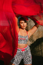 Load image into Gallery viewer, Woman wearing a black and white Koko Active leopard print patterned sports bra with red accents, holding red fabric.
