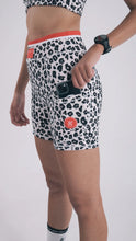 Load image into Gallery viewer, A person wearing Koko Active&#39;s Extra Shorty Shorts - Step Up, featuring ethically produced leopard print with a red waistband and logo, carries a phone in their pocket and sports a watch. The sleek outfit pops against the white background while offering style and UV50 protection.
