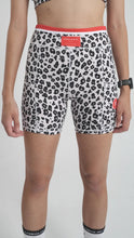 Load image into Gallery viewer, Flaunting Koko Active’s ethically produced black and white leopard print sports bra and Extra Shorty Shorts - Step Up with a red waistband, UV50 protection enhances the chic look. A smartwatch complements the ensemble against a plain background.
