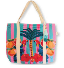 Load image into Gallery viewer, The Beach Bag - Frangipani Parrots by Natural Selection is a colorful tote crafted from poly canvas, showcasing beige handles, a vibrant palm tree design with parrots, oranges, and pink hibiscus on pink and teal stripes. It features waterproof lining and a tassel charm on one handle.
