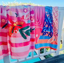 Load image into Gallery viewer, Various sarongs hanging over a railing by Natural Selection featuring colourful illustrations in bright colours. Each sarong beach wrap is made from crepe fabric and comes with a matching wet bag.
