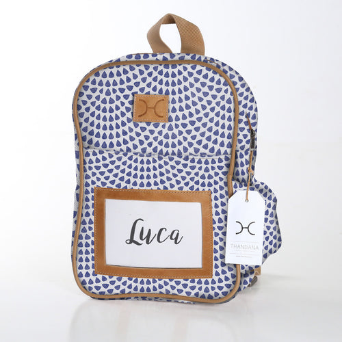 Thandana kids' backpack with a blue geometric pattern, brown leather straps, and a name tag displaying 'Luca'.