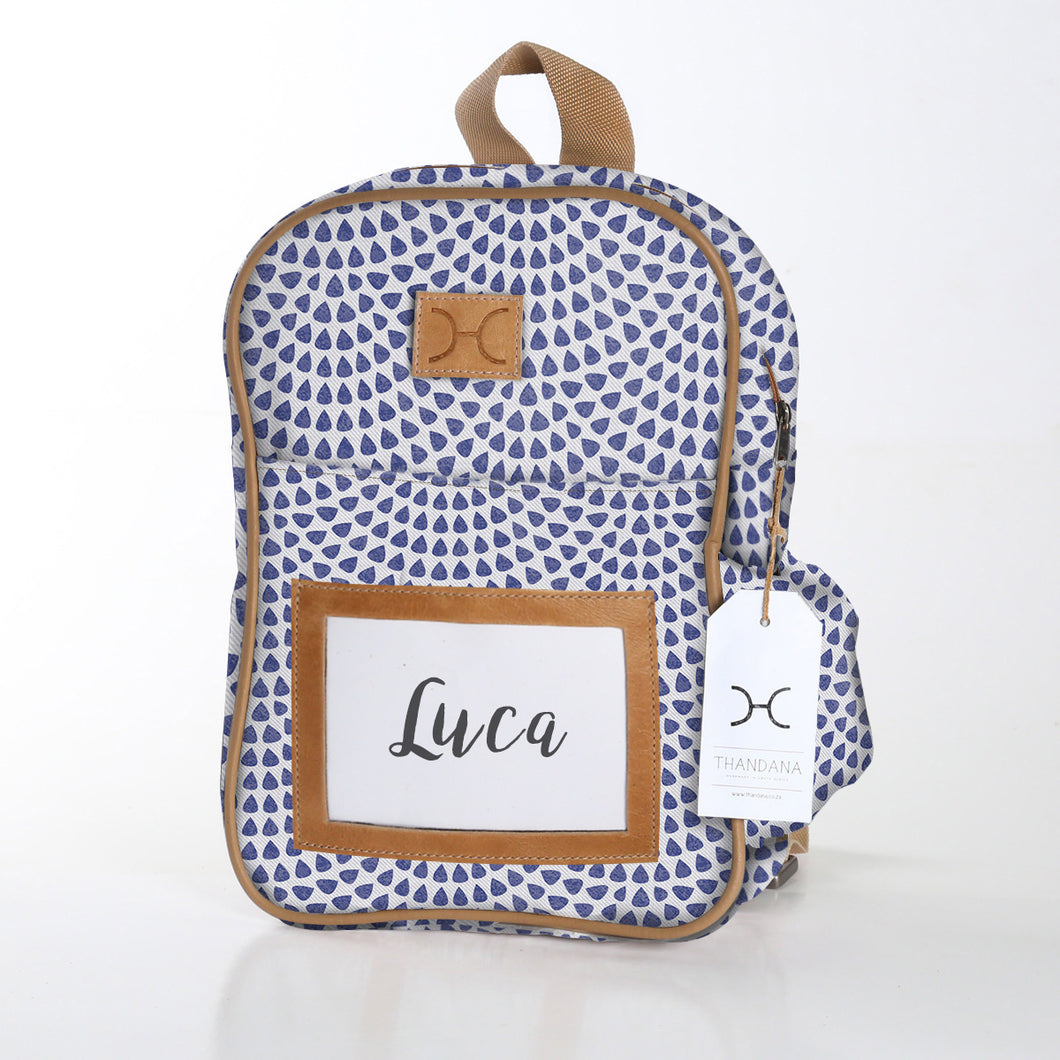 Thandana kids' backpack with a blue geometric pattern, brown leather straps, and a name tag displaying 'Luca'.